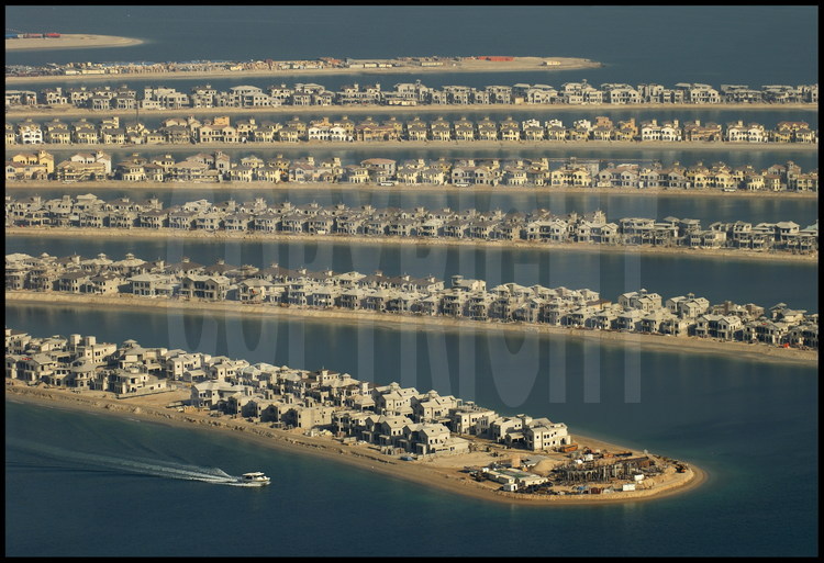 Mai 2006. Chantier off shore du “Palm Jumeirah”. Avec ses 3 840 km2, Dubaï n’a qu’une courte façade littorale. Aussi, le petit émirat s’est-il lancé à partir de 2001 dans de pharaoniques projets touristiques, dans le dessein d’augmenter ses côtes en construisant les plus importantes îles artificielles du monde. Premier du genre, le « Palm Jumeirah » est un ensemble gagné sur la mer constitué d’un tronc et de 17 palmes cerclée par une digue longue de 11 km. Sur cet ensemble de 5 km de diamètre, 60 kilomètres de plages ont été créés en déplaçant plus de 100 millions de m3 de sable et de rochers. Inititialement prévu pour être achevé fin 2006, le chantier a pris du retard. Le « Palm Jumeirah» accueillera plusieurs dizaines d’hôtels, des milliers de maisons individuelles et d’appartements ainsi que des marinas, des restaurants, des parcs aquatiques, des centres commerciaux, des terrains de sport, des centres de thalassothérapie, des cinémas, etc. Un pont de 300 mètres reliera le tronc au continent, tandis qu'un monorail desservira le coeur du complexe, constitué d’un hôtel de 1 000 chambres et d’un parc aquatique.