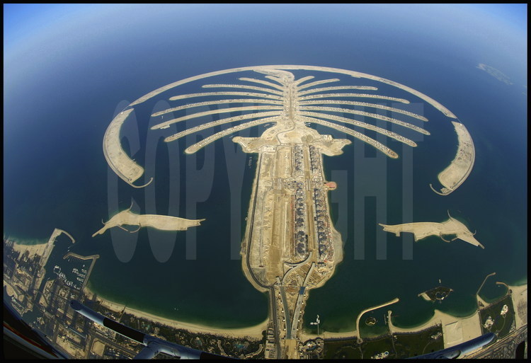 Juin 2006. Chantier off shore du “Palm Jumeirah”. Avec ses 3 840 km2, Dubaï n’a qu’une courte façade littorale. Aussi, le petit émirat s’est-il lancé à partir de 2001 dans de pharaoniques projets touristiques, dans le dessein d’augmenter ses côtes en construisant les plus importantes îles artificielles du monde. Premier du genre, le « Palm Jumeirah » est un ensemble gagné sur la mer constitué d’un tronc et de 17 palmes cerclée par une digue longue de 11 km. Sur cet ensemble de 5 km de diamètre, 60 kilomètres de plages ont été créés en déplaçant plus de 100 millions de m3 de sable et de rochers. Inititialement prévu pour être achevé fin 2006, le chantier a pris du retard. Le « Palm Jumeirah» accueillera plusieurs dizaines d’hôtels, des milliers de maisons individuelles et d’appartements ainsi que des marinas, des restaurants, des parcs aquatiques, des centres commerciaux, des terrains de sport, des centres de thalassothérapie, des cinémas, etc. Un pont de 300 mètres reliera le tronc au continent, tandis qu'un monorail desservira le coeur du complexe, constitué d’un hôtel de 1 000 chambres et d’un parc aquatique.