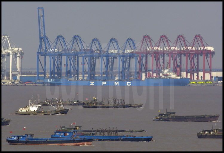 Situé sur la rive sud de l’île de Changxing Dao, près du village de Zhenhua, la manufacture d’équipement portuaires du ZPMC (Zhenhua Port Machine Company). Cette entreprise a exporté en 2005 plus de 1500 portiques dans 70 ports de 37 pays, ce qui représente près de 60% du marché mondial. C’est d’ailleurs cette compagnie qui a fourni les portiques pour les nouveaux quais du port du Havre, en France, destinés à accueillir les porte-containers géants de 8000 EVP et plus. En avant plan, le bras sud de l’estuaire du Yang Tse Kiang.