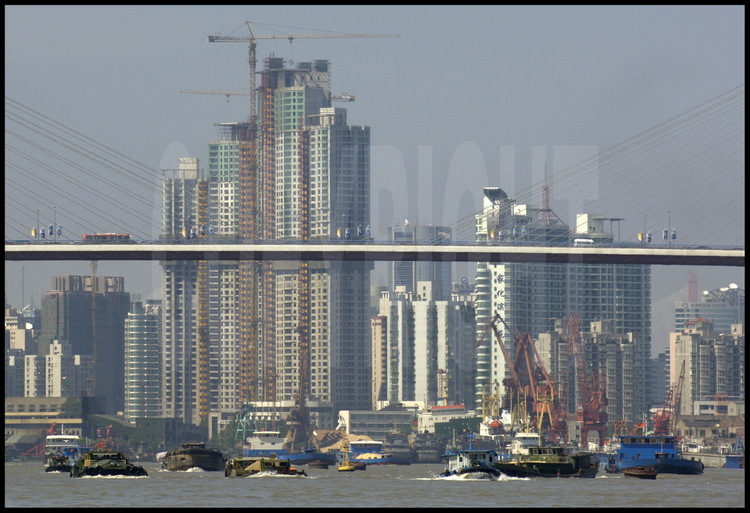 Dans le centre ville de Shanghai, trafic de péniches le long de la Huang Pu river, avec des installations portuaires, le pont Nanpu et de nouvelles tours d’habitations de la ville de Pudong (qui signifie « à l’est du Pu ») en arrière plan.