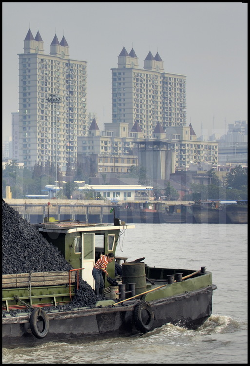 Dans le centre ville de Shanghai, péniche transportant du charbon navigant sur la Huang Pu river. En arrière plan, des tours d’habitation de la ville de Puxi (qui signifie « à l’ouest du Pu).