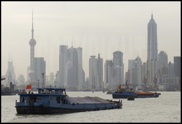 Dans le centre ville de Shanghai, péniches navigant sur la Huang Pu river, avec les tours de la nouvelle ville de Pudong (qui signifie « à l’est du Pu ») en arrière plan, la tour TV « Perle de l’Orient » à gauche et la tour Jinmao à droite. .