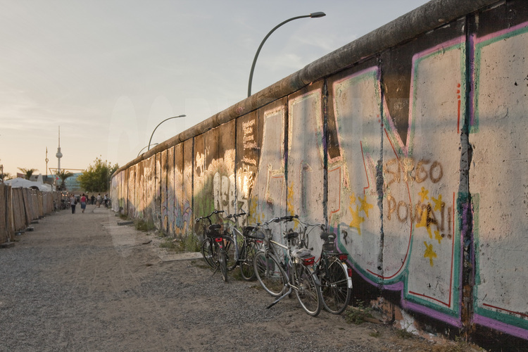 L’East Side Gallery. Située sur la Mühlenstrasse, dans le quartier de Friedrichshain, c’est le plus grand segment de mur conservé. Long de 1300 mètres et classé monument historique en 1992, c’est également devenu la plus grande galerie en plein air au monde. Avant 1989, le mur était de couleur blanche et grise, une barrière empêchait de l’approcher ou de le toucher. L’intégralité du fleuve, qui faisait office de «no man’s land», faisait partie de Berlin-Est et était arpenté par les patrouilleurs des gardes-frontières. De nombreux berlinois périrent noyés en tentant de passer à l’ouest. A cette époque, la Mühlenstraße faisait partie de l’itinéraire «protocolaire» des dirigeant est berlinois, entre le centre ville et l’aéroport de Schönefeld. C’est pourquoi elle fut délimitée par un segment de mur extérieur (appelé «mur occidental» par les autorités de RDA), afin de cacher le No Man’s Land. L’autre partie du mur se dressait le long de la berge, ces derniers dissimulant le dispositif habituel comprenant la clôture de signalisation, le chemin de ronde, les pylônes d’éclairage ainsi que des barbelés près de l’eau. Après la chute du mur, 118 artistes originaires de 21 pays commencèrent à peindre une gigantesque fresque sur la face est du mur, intouchée du temps de l'Allemagne divisée. Certaines de ces œuvres sont depuis devenues des icônes, tel le baiser échangé entre Leonid Brejnev et le dirigeant de la RDA Erich Honecker et la série de «dialogues» du français Thierry Noir. Mais en vingt ans, la pollution, les graffitis et l’usure du temps avaient failli détruire à jamais ces peintures, qui ont pris depuis une valeur patrimoniale considérable. C’est pourquoi la ville de Berlin a pris l’initiative de convier, durant l’été 2009, quarante artistes de l'époque, venus du monde entier, qui ont été invités cet été à reproduire trait pour trait leur œuvre telle qu’ils l’avaient crée il y a vingt ans. Le message de cette œuvre d’art urbain est celui de l’euphorie qui régna au lendemain de la chute du mur.
