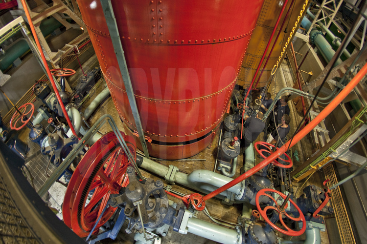 Au sous-sol du pilier est de la Tour Eiffel, des techniciens de la SETE assurent la maintenance de la machinerie d'ascenseur de 1889, toujours en fonctionnement. En rouge au centre, l'un des accumulateur du système (voir image n° 106).