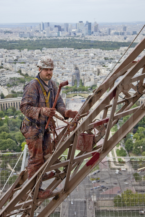 A 250 m d'altitude sous le troisième étage de la Tour Eiffel, le peintre-alpiniste Florin Vieriu applique une couche d'antirouille (rouge) sur la face nord-ouest du monument. En arrière plan, les jardins et le palais du Trocadéro, le 16° arrt. de Paris, le bois de Boulogne et la quartier de la Défense. .