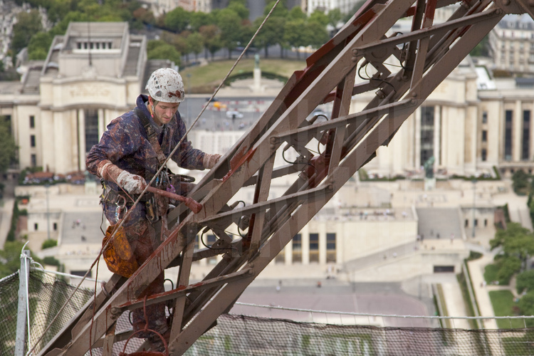 A 230 m d'altitude sous le troisième étage de la Tour Eiffel, le peintre-alpinistes Edouard Saunier applique une couche d'antirouille (rouge) sur la face nord-ouest du monument. En arrière plan, le palais et l'esplanade du Trocadéro.