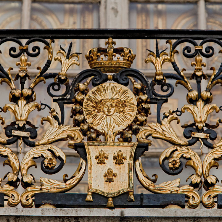 Cour de marbre. Sur la grille du balcon de la chambre du Roi, emblèmes royaux : tête d’Apollon ornée de guirlandes fleuries, fleurs de lys et couronne.