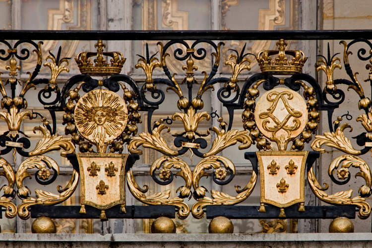 Cour de marbre. Sur la grille du balcon de la chambre du Roi, emblèmes royaux : tête d’Apollon ornée de guirlandes fleuries, fleurs de lys et couronne.