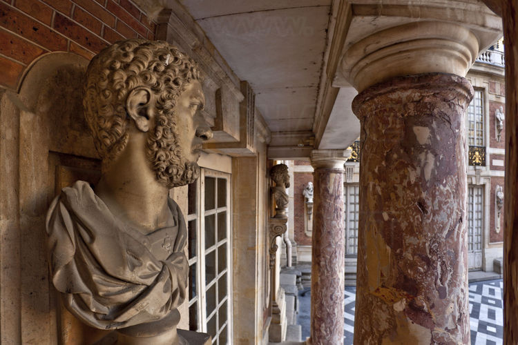 Cour de Marbre. Sous le balcon du Roi, le carrare blanc s'utilise pour les encadrements, faisant ressortir les colonnes de marbre jaspé de blanc et de rouge. A gauche, un des quatre-vingt quatre bustes à l’antique des cour Royale et cour de Marbre.