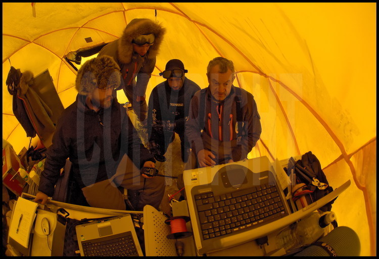 Sous la tente de terrain, à quelques pas du trou creusé sous la banquise, le créateur du ROV  (Remote Operating Vehicle) Denis BOURGAL (à gauche) et l'ingénieur Jérôme Boutain (à droite)  recueillent et analysent les premières données envoyées par le ROV. Au centre, les plongeurs Guislain Bardout et Samuel Audrain (en combinaison).