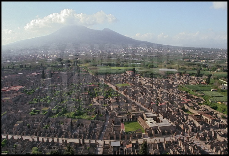 Vue aérienne de la partie centrale de Pompéi. Au premier plan à droite, le carrefour des deux artères principales de la ville antique, la Via del Vesuvio et la via dell’Abondanza, où se trouve également les thermes de Stabies. En arrière plan, le Vésuve.