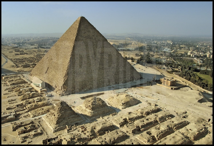 La Pyramide de Kheops (IVème dynastie) vue depuis sa façade Est. Au premier plan, les mastabas orientaux de la nécropole. Au second plan, les trois Pyramides des Reines attachées à Kheops. Au troisième plan à gauche,  la Barque Solaire, découverte sous les sables en 1954 et aujourd’hui abritée dans son musée.