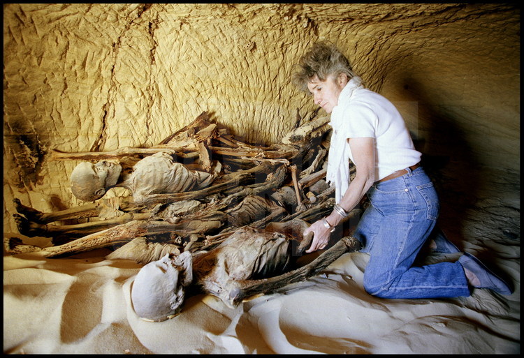 Site d'Ain Labakha. Chaque tombe renfermait plusieurs momies, parfois une dizaine, gisant alignés sur la sable. Certains corps, momifiés selon les rites égyptiens, avaient conservés les bandelettes qui les recouvraient.  Il a par la suite été prouvé que tous les corps appartenaient à une même famille. Au premier plan, l'historienne Françoise Dunand.