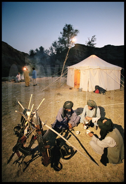 Campement de l’expédition, près du site de Lundo. Comme toutes les nuits, les gardes Bugtis veillent. Au deuxième plan, assemblés en pyramide, les fusils mitrailleurs  des gardes. Au premier plan, la grande tente commune, qui sert aux repas pendant la journée et à l’examen des fossiles la nuit venue.