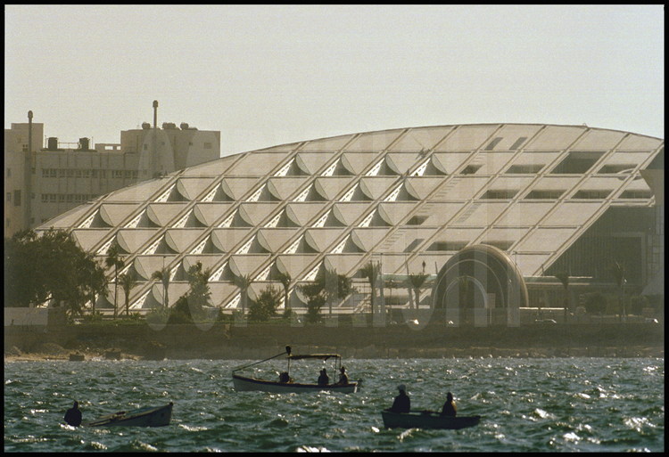 La Biblioteca Alexandrina vue depuis le fort Qaït Bey (site antique du phare d'Alexandrie). Les pêcheurs alexandrins du port Est naviguent à proximité de l'édifice.