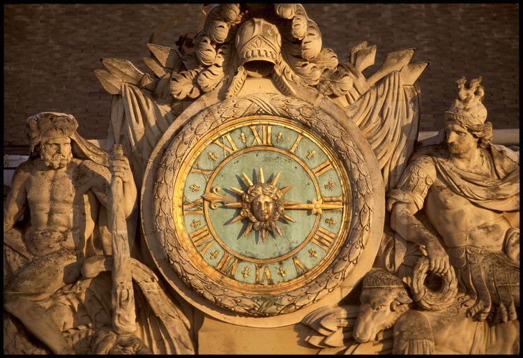 La grande horloge du Château, surmontée de casque, drapeaux et tores de lauriers. Les éléments sculptés situés à gauche et à droite représentent la France se reposant après sa victoire sur ses ennemis, symbolisés par le dragon. A gauche, Hercule assis sur un dragon. A droite, Mars et un bélier au repos.