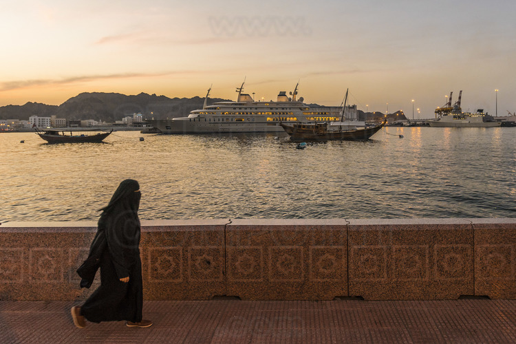 Oman. Mascate : Jeune femme sur la corniche de la ville. En arrière plan, le yacht du Sultan Al Qaboos. // Oman. Muscat: Young woman on the cornice of the city. In the background, the yacht of Sultan Al Qaboos.