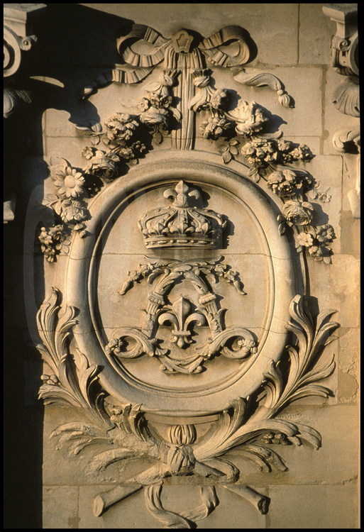Sur la façade sud de la Chapelle, détail d’un bas-relief représentant un médaillon entourant deux L entrelacés et couronnés. C’est le chiffre du Roi Soleil.