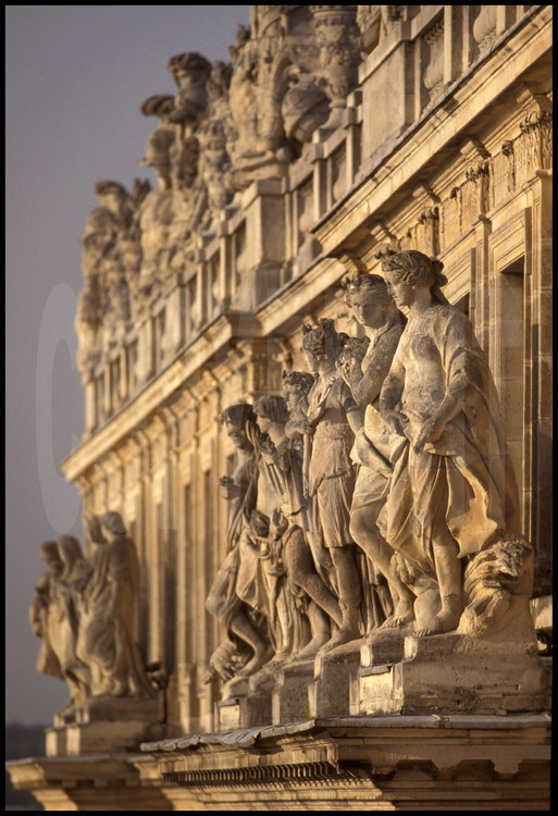 La balustrade de l’avant-corps central avec ses trophées d’armes et ses vases dissimulant les toits. Au premier plan, les statues représentant les Mois de l’année entourant Diane et Apollon.