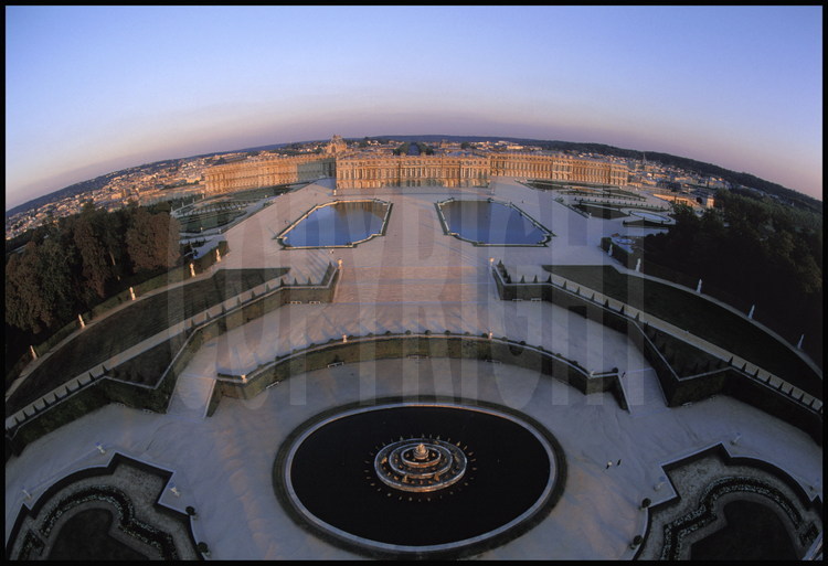 Vue générale aérienne de la façade ouest du Château de Versailles et de ses jardins à la française. Au premier plan, le Bassin de Latone, au second plan, les Parterres d’eau puis le corps central flanqué de l’aile du Nord et de l’aile du Midi.