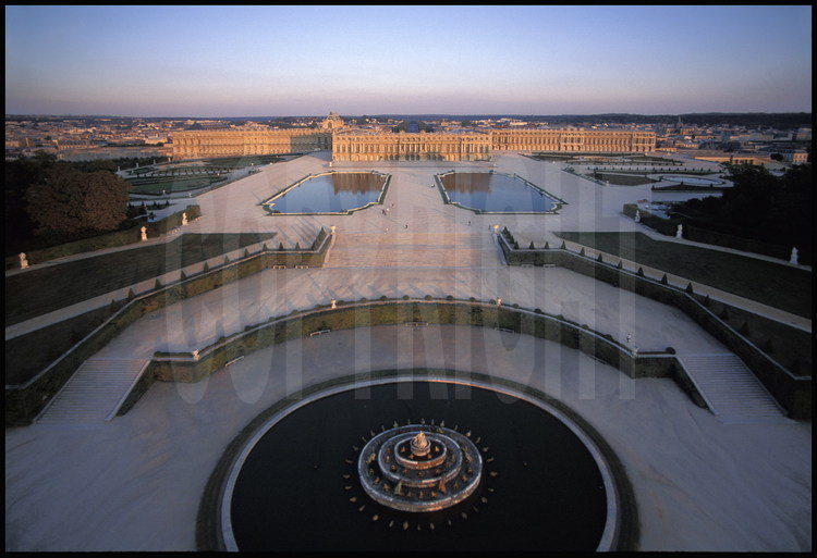 Vue générale aérienne de la façade ouest du Château de Versailles et de ses jardins à la française. Au premier plan, le Bassin de Latone, au second plan, les Parterres d’eau puis le corps central flanqué de l’aile du Nord et de l’aile du Midi.