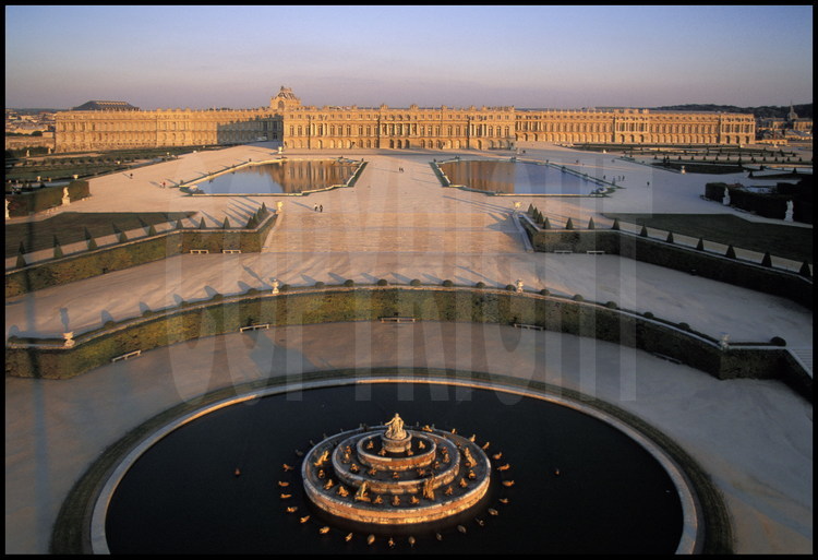Vue générale de la façade ouest du Château de Versailles et de ses jardins à la française. Au premier plan, le Bassin de Latone, au second plan, les Parterres d’eau puis le corps central flanqué de l’aile du Nord et de l’aile du Midi.