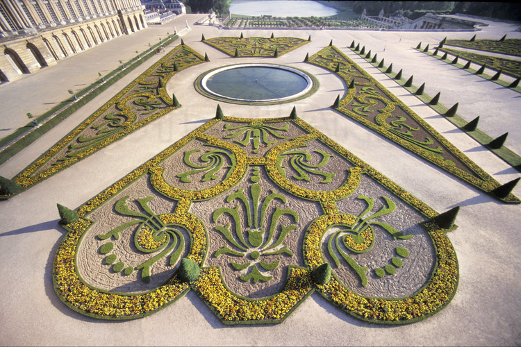 Décorations de buis sur le parterre du Midi dessiné par Le Nôtre avec, au premier plan, la fleur de lys, symbole de la royauté. En arrière plan, l’Orangerie et la pièce d’eau des Suisses.
