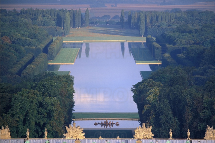 La grande perspective et l'Axe du Soleil du parc de Versailles depuis l'est. Au premier plan, les trophées d’armes de la balustrade du toit, suivis du Bassin d’Apollon et du Grand Canal.
