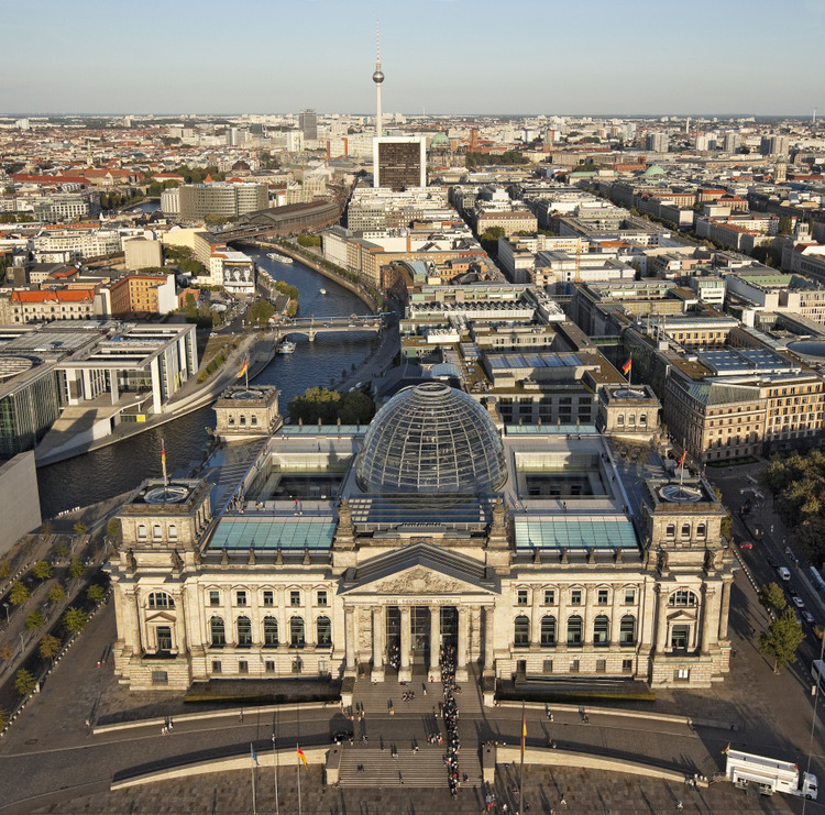 Reichstag et Bundestag.  Le tracé du mur jouxtait la face est du Reichstag. Conséquence de la réunification de l’Allemagne le 3 octobre 1990, le Bundestag (Diète Fédérale d’Allemagne) décidait, un an plus tard, de faire du Reichstag le siège du parlement à Berlin, la capitale restaurée de l’Allemagne réunifiée. Après une restauration complète du bâtiment original de 1894, le Bundestag se réunit en ce lieu le 19 avril 1999, dans un bâtiment spectaculairement restauré par Norman Foster. Le Reichstag a souffert de nombreuses dégradations et de destructions au cours du 20ème siècle. Apres la réunification et le transfert du Bundestag de Bonn à Berlin, il devint nécessaire d’équiper et de moderniser complètement le bâtiment languissant. L’architecte britannique Sir Norman Foster fut chargé de mener à bien le gigantesque projet de transformation, comprenant la désormais célèbre coupole en verre. La réunification officielle de l’Allemagne fut célébrée ici le 2 octobre 1990. Plus récemment, durant l’été 1995, les Berlinois et les visiteurs du monde entier affluèrent pour admirer l’expérience de l’emballage du Reichstag par l’artiste Christo. L’événement magique dura deux semaines comme un dernier adieu avant le début des travaux de restauration.
