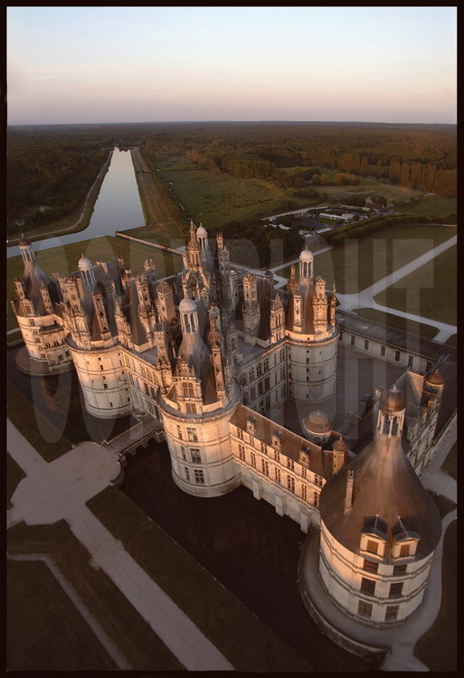 A l'aube, les toits du château de Chambord vus depuis le Nord Ouest. En arrière plan, le Cosson. Classé au patrimoine mondial de l'Unesco depuis 1981, Chambord est le plus vaste des châteaux du val de Loire et constitue l'un des chefs-d'œuvre architecturaux de la Renaissance : 156 m de façade, 426 pièces, 77 escaliers, 365 cheminées et 800 chapiteaux sculptés.