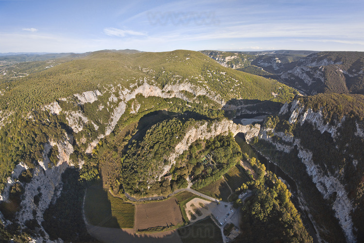 Vue générale de la combe d'Arc, où est situé la grotte Chauvet originelle. Datée de 36000 ans, la grotte Chauvet fut découverte en décembre 1994 et immédiatement fermée au public en raison de son immense intérêt scientifique et à une forte présence de dioxide de carbone. Sur ses parois, les œuvres des premiers artistes de l'Histoire. A droite, le Pont d'Arc et la rivière Ardèche. En arrière plan à l’extrême gauche, le site de la Caverne du Pont d'Arc, sur le site du Razal.