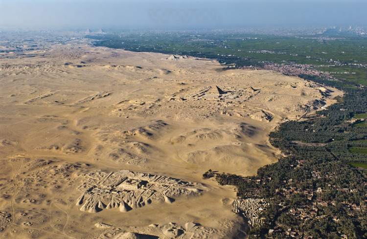 A l’ouest du ruban fertile de la vallée du Nil, vue aérienne du plateau de Sakkâra, aujourd’hui un désert d’où surgissent les vestiges du passé. Au nord, (a fond à gauche), se trouve le plateau de Gizeh avec les trois fameuses pyramides de la IV dynastie : Kheops, Khephren et Mykérinos. Puis les trois petites pyramides d’Abousir. Au centre, sur le site de Saqqarah, la célèbre pyramide à degrés de Djoser, datant de la III dynastie (plus ancien monument en pierre de l’histoire de l’humanité). Juste à droite, la pyramide de Téti, prédécesseur d’Ouserkarê. Au sud (premier plan), le complexe funéraire de Pépy Ier, fouillé par les archéologues français J. Leclant et A. Labrousse. Entre les sites de Djoser et de Pépy Ier, le site de Tabbet al-Guech où l’équipe de l’archéologue Vassil Dobrev fouille pour retrouver la trace du pharaon disparu, Ouserkarê. Malgré la sensation d’incompréhension qu’inspire pareille étendue, les archéologues perçoivent de mieux en mieux l’agencement de ces colossales nécropoles construites suivant des axes se recoupant les uns avec les autres.