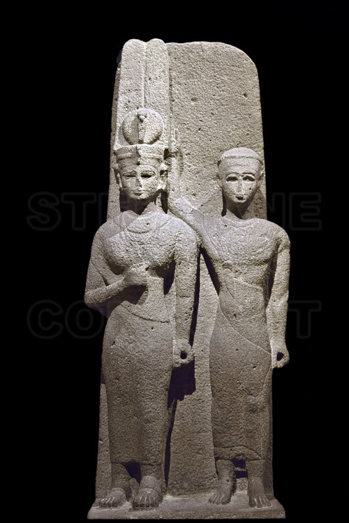 Found in Meroe, this double statue in basalt shows a queen and a prince each wearing a Meroitic costume with the sash drapped over the right shoulder. The prince is raising his right arm behind the head of the queen as is supporting her tall crown. Their eyes were inlaid, something rare in Kushite art. Both were holding in their hands an object now missing. 2nd century AD.