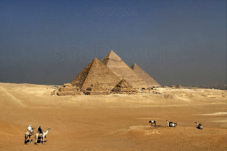 Depuis le désert de Libye, à l’Ouest du Caire, la célèbre vue dite des « neufs pyramides » : au premier plan, les trois petites pyramides des reines de Mykérinos. Derrière, les pyramides de Mykérinos, Khephren et Kheops. A droite de cette dernière, les trois petites pyramides des reines de Kheops. Toutes sont de la IVème dynastie. En arrière plan à droite, la ville du Caire.