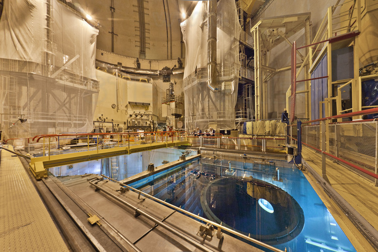 Centrale nucléaire du Bugey : Vue générale de l'intérieur du bâtiment du réacteur n° 4 (étage supérieur) et du couvercle interne supérieur de la cuve qui est sous eau dans la piscine (la cuve est en contre bas dans l'autre partie de la piscine du bâtiment réacteur -cette partie est aussi appelée : internes supérieurs-) . Avec son couvercle, celle-ci pèse 300 tonnes, pour un diamètre de 4 mètres et une hauteur totale de 13 mètres. L'épaisseur des parois est au minimum, de 20 cm d'acier forgé recouvert d'un revêtement inoxydable. En arrière plan à gauche, la journaliste du Figaro magazine Martine Betti-Cusso entourée de Thierry Clément, responsable des arrêt de tranche et de Serge Blond, directeur adjoint du site. Pour éviter tout risque de radiations, la piscine du réacteur est remplie d’eau borée, piège à neutrons.