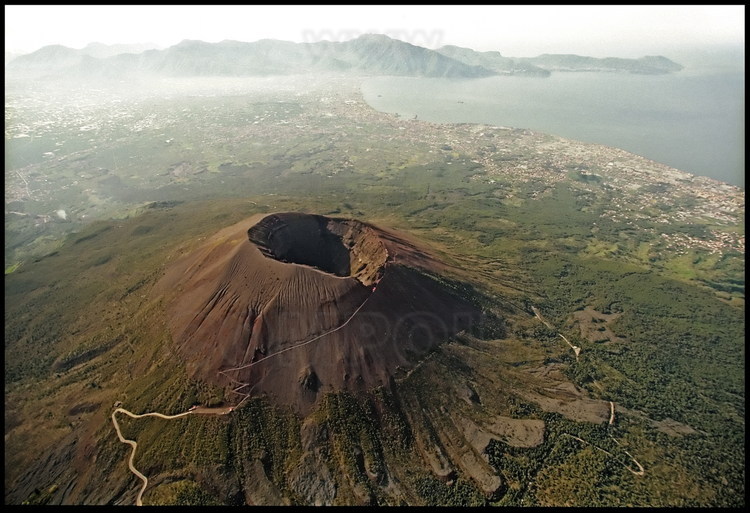 Le Vésuve, qui culmine à 1270 mètres. Tout autour, des traces de laves dues aux multiples éruptions (sept depuis 1631). En arrière plan, la baie de Naples et les villes qui se pressent sur la côte.
