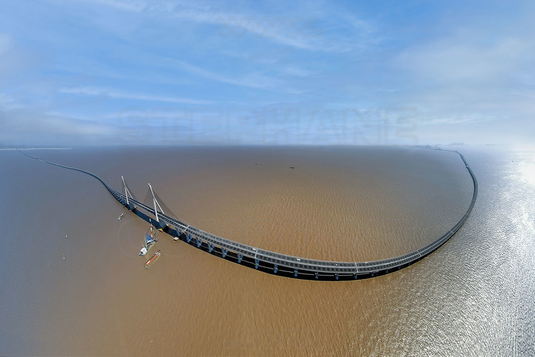 Panorama complet des 32,5 kilomètres du pont de Donghai. A l’extrême gauche, la côte de Luchao, en direction de Shanghai. A gauche, le pont suspendu central, qui permet le passage -avec sa hauteur de 40 mètres sous tablier- des plus gros navires depuis la baie de Hangzhou vers la mer de Chine orientale. Au centre, le tablier du pont à hauteur du point kilométrique 17 (le km 0 est à gauche). A droite, l’archipel des îles Yangshan, sur lequel a été construit le port en eaux profondes éponyme. La couleur de la mer est due à une pluie d'orage tombée quelques heures auparavant, qui a également provoqué une transparence de l'air inhabituelle. Cette image aérienne a été réalisée –comme toutes celles de ce reportage- à l’aide d’un ballon à hélium radio-commandé depuis la mer.