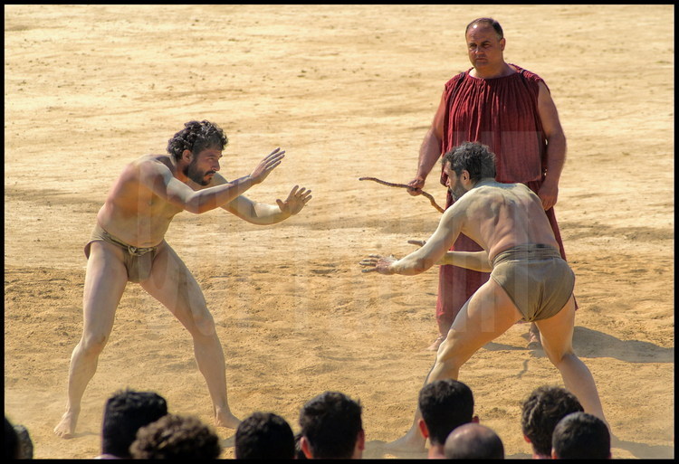 Pierre Dufour (left) and Brice Lopez (right), athletes-researchers in experimental archaeology, compete in the pancratium competition under the watch of Greek hellanodice judge-referee Christos Kollias. As this event has no time limit, the combat is over only when one of the pancratists gives up.
