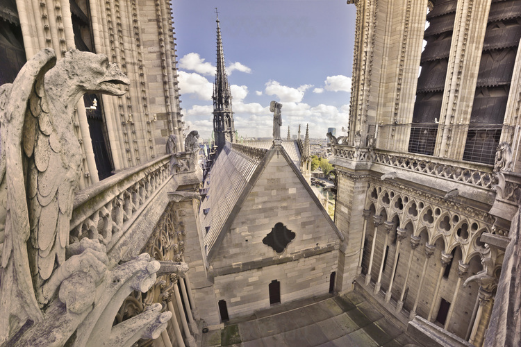 Paris (75) - Cathédrale Notre Dame de Paris :  ntre les deux tours, l'etroit passage permet d'admirer la perspective sur les pentes abruptes du toit recouvrant la charpente de la nef. Il est surmonte de la fleche, qui culmine a 93 metres a la croisee des transepts. Le pignon ouest du toit de la nef est surmonte d'un ange musicien (gros plan photo 15). La grande galerie qui court le long de la base des tours est ornee de chimeres imaginees et disposees par Viollet le Duc au XIXe siecle. Altitude 40 metres. // France - Paris (75) - Cathedral Notre Dame de Paris : Between the two towers, the narrow passage allows to admire the view on the steep slopes of the roof covering the structure of the nave. It is surmounted by the arrow, which rises to 93 meters at the transept crossing. The west gable of the roof of the nave is surmounted by an angel musician (closeup photo 15). The large gallery that runs along the base of the tower is decorated with chimeras imagined and disposed by Viollet le Duc in nineteen century. Altitude 40 meters.