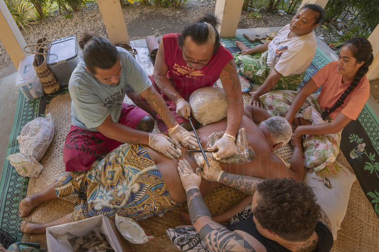 Iles Samoa américaines (anciennes Samoa orientales) - Ile de Tutuila : Tatouage traditionnel dans le village de Poloa. Le maître tatoueur, M. Wilson Fitiao (t-shirt rouge) est l'un des rares à avoir le droit d'exercer cet artisanat ancestral, contrôlé par quelques familles. Aux Samoa, le tatouage est un marqueur social fort, signe d'honneur et de respect. Bien qu'il ne soit pas obligatoire, presque tous les chefs de villages en portent, y compris les femmes. C'est le tatoueur (et non le 
