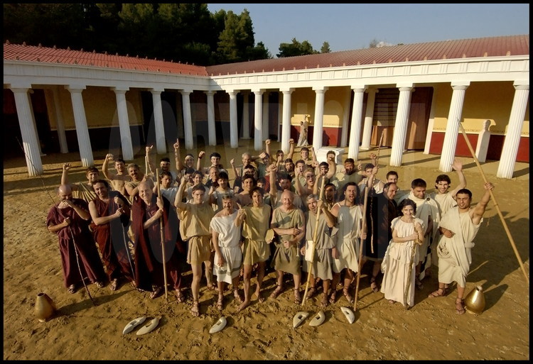 Dans la cour de la palestre, portrait de groupe de tous les athlètes, entraîneurs et archéologues (dans le rôle des juges-arbitres dits hellanodices) participant aux compétitions dans le stade antique d’Olympie.
