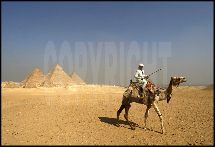 Depuis le désert de Libye, à l’Ouest du Caire, la célèbre vue dite des « neufs pyramides »: au premier plan, les trois pyramides des reines de Mykérinos. Derrière, les pyramides de Mykérinos, Khephren et Kheops. A droite de cette dernière, les trois pyramides des reines de Kheops. Toutes sont de la IVème dynastie. En arrière plan à droite, la ville du Caire.