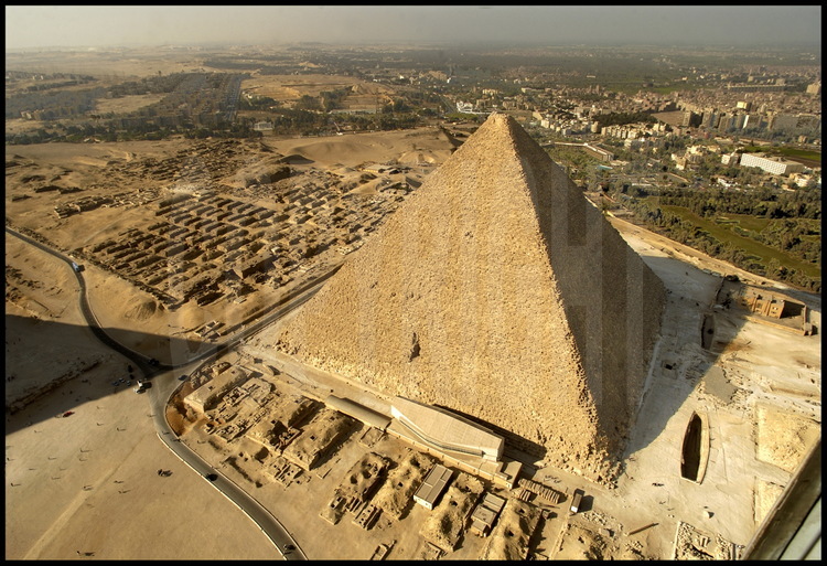 Au premier plan, la Barque Solaire, découverte sous les sables en 1954 et aujourd’hui abritée dans son musée. Au second plan, la pyramide de Kheops (IVème dynastie). En arrière plan à gauche, les mastabas occidentaux de la nécropole. En arrière plan à droite, la ville du Caire.