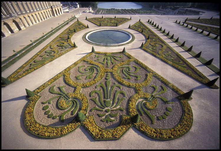 Décorations de buis sur le parterre du Midi dessiné par Le Nôtre avec, au premier plan, la fleur de lys, symbole de la royauté. Au fond, l’Orangerie et la pièce d’eau des Suisses.