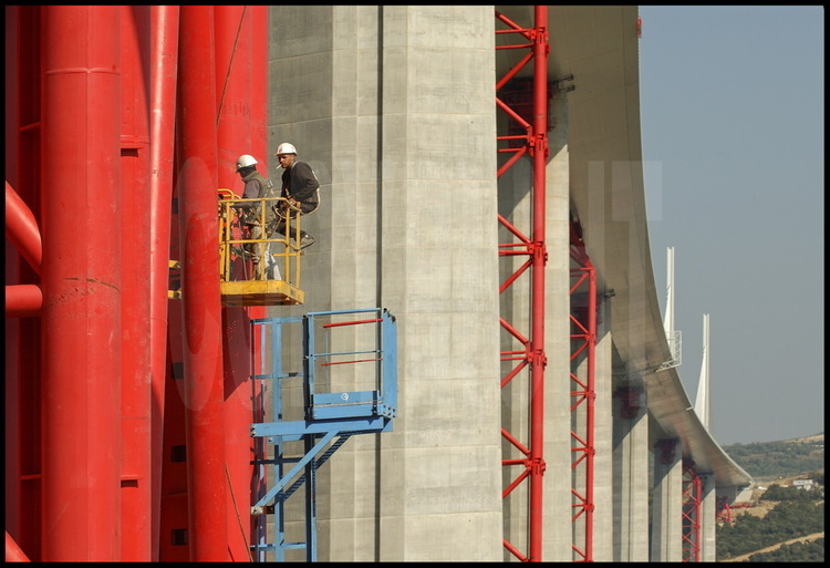 Sous le tablier du Viaduc, des ouvriers commencent le démontage des palées intermédiaires (en rouge) qui ont permis le soutien du pont durant toute sa construction.