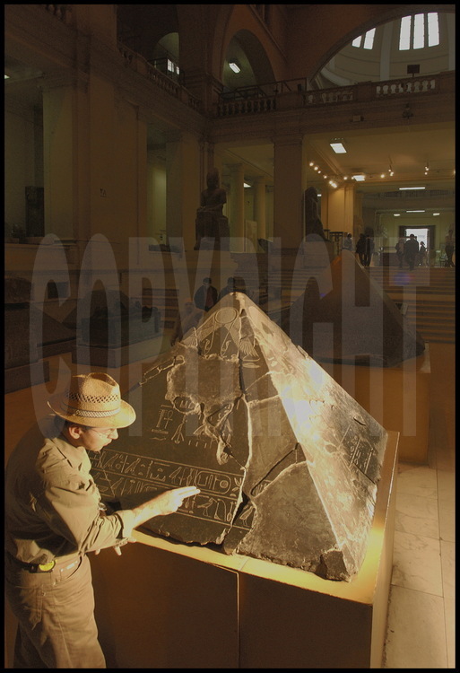 Au Musée Egyptien du Caire, l’archéologue français Vassil Dobrev observe le pyramidion (ultime pierre coiffant la pointe d’une pyramide) provenant de la pyramide du roi Khendjer. Ce pharaon de la XIII dynastie (Moyen Empire) a fait construire sa pyramide à l’extrémité sud du site de Saqqâra-Sud. Nommé Khendjer « fils de Rê », il porte un deuxième nom : Ouserkarê « roi de Haute et Basse Egypte ». D’après Vassil Dobrev, pointant ici le cartouche en question, ce deuxième nom fait référence à son lointain ancêtre, Ouserkarê, deuxième roi de la VI dynastie, ayant régné deux courtes années, entre 2323 et 2321 avant J.C (Ancien Empire).
