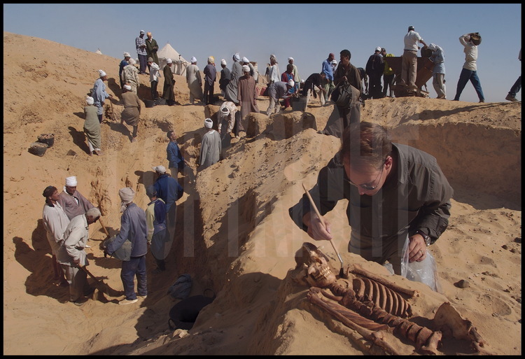 Quentin Vandevelde, membre de la mission de l’I.F.A.O. de Tabbet-al-Guech, est en train de dégager le squelette d’un adulte enterré directement dans le sable. Sur tout le périmètre de la fouille, les archéologues ce cessent d’exhumer squelettes et momies. Cette abondance de corps confirme l’étendue de cette nécropole de l’époque saïte.