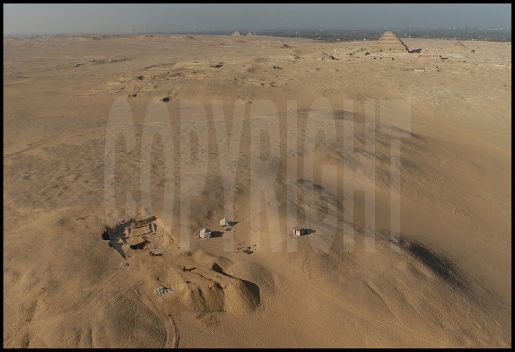 Aerial view of the plateau of South Saqqara. In the center is the site of Tabbet al-Guesh where archeologist Vassil Dobrev and his team are searching for clues to the lost pharaoh, Userkare. Despite the apparent incomprehensible vastness of such a space, researchers are increasing their understanding of the layout of these colossal necropoli, which were built following strict axial guidelines. In the background to the left, is the plateau of Gizeh with the three famous pyramids of the IVth dynasty: Kheops, Khephren and Mykerinos. In the background in the center are the three small pyramids of Abu Sir. To the right is the famous Step Pyramid of Djoser, dated to the IIIrd dynasty. Far right is the pyramid of Teti, Userkare’s predecessor.